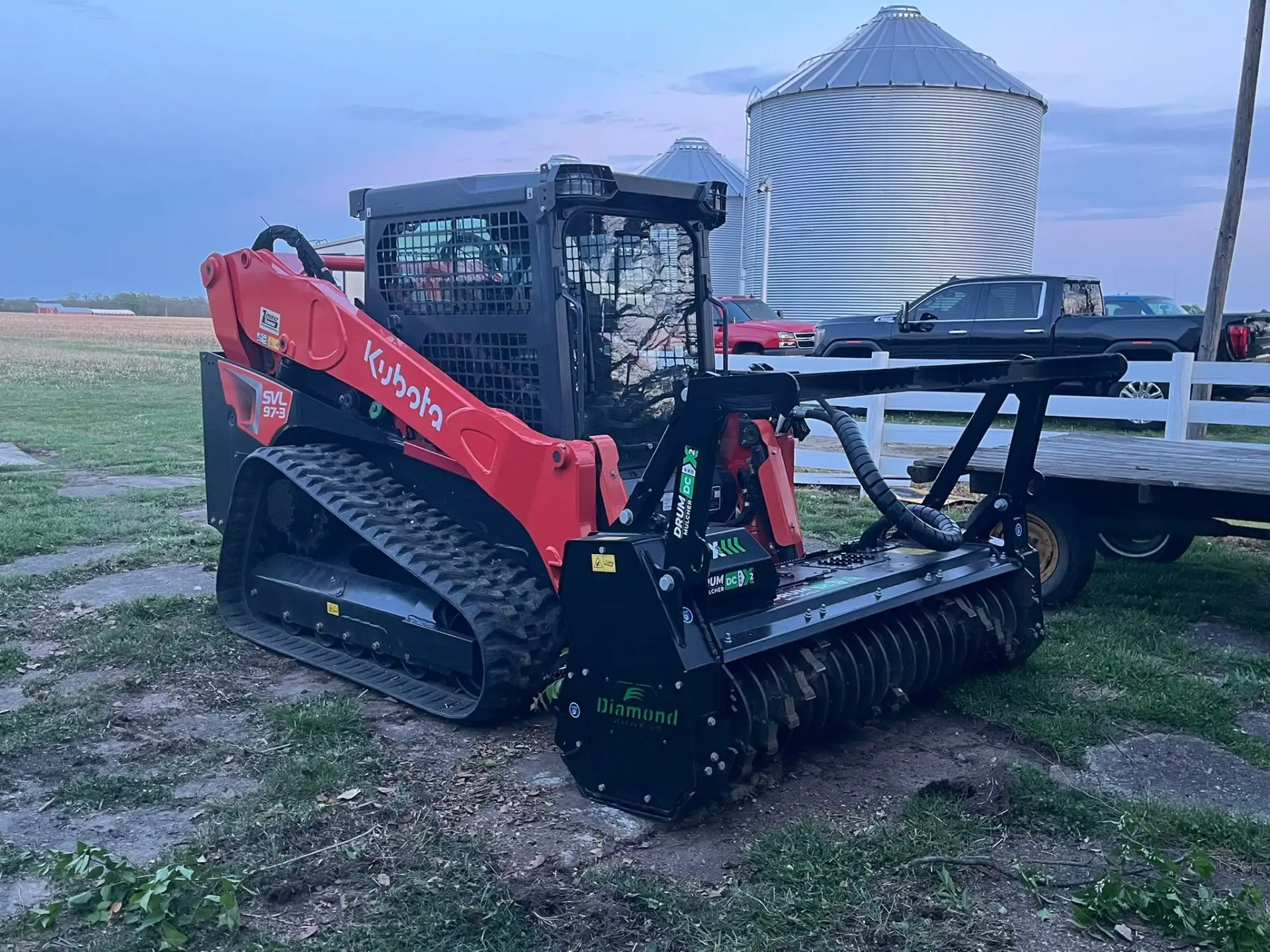 Kubota track loader with a forestry mulcher clearing brush on an Ohio property at dusk